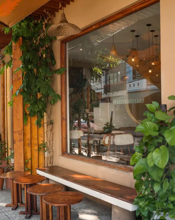 Ghế đẩu gỗ dọc ô cửa kính lớn phủ dây leo trước quán